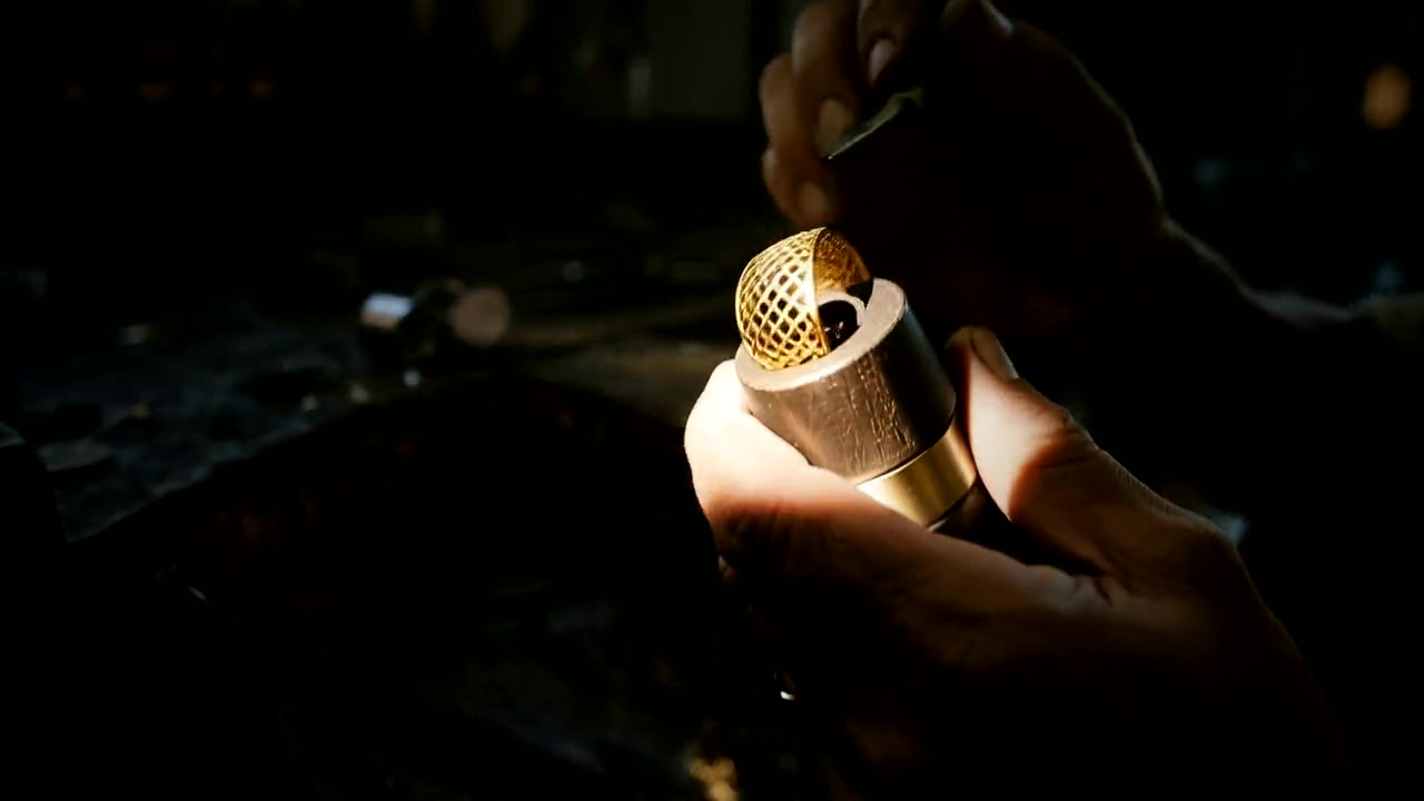 A jeweller’s hands holding a gold piece in the half-light of the atelier
